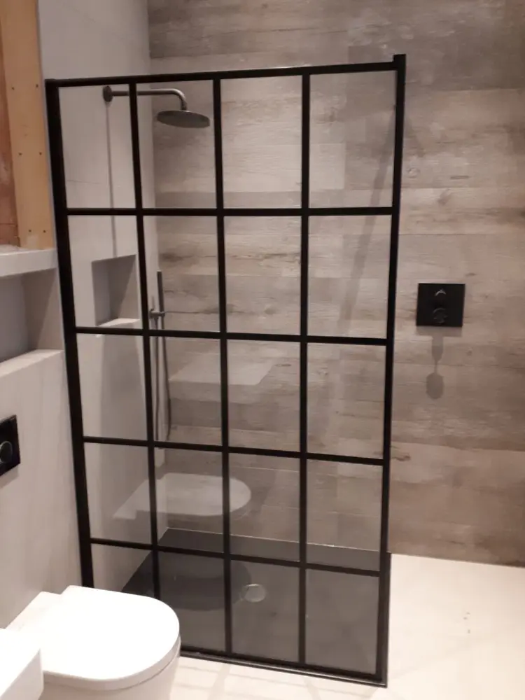 Nowoczesna łazienka z kabiną prysznicową z czarną szklaną ramą, ścienną słuchawką prysznicową i toaletą.