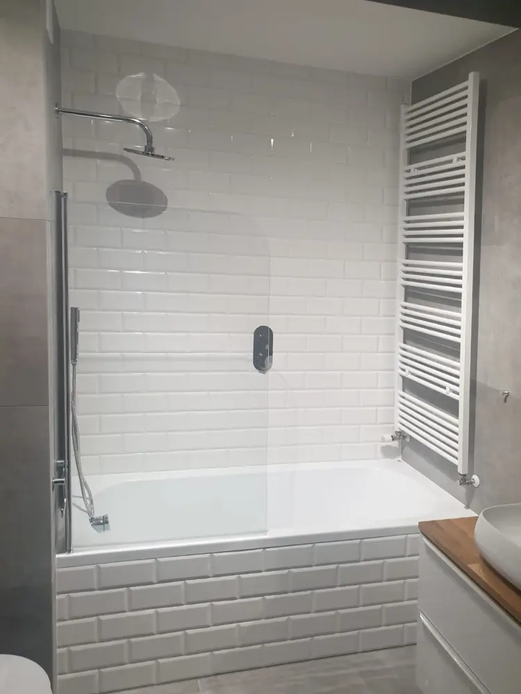 Nowoczesna łazienka z białymi płytkami z cegły, przeszkloną wanną, prysznicem i pionowym grzejnikiem.