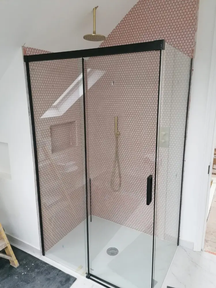 Nowoczesny prysznic ze szklanymi drzwiami, złotymi elementami wyposażenia i różowymi wzorzystymi płytkami na ścianie.